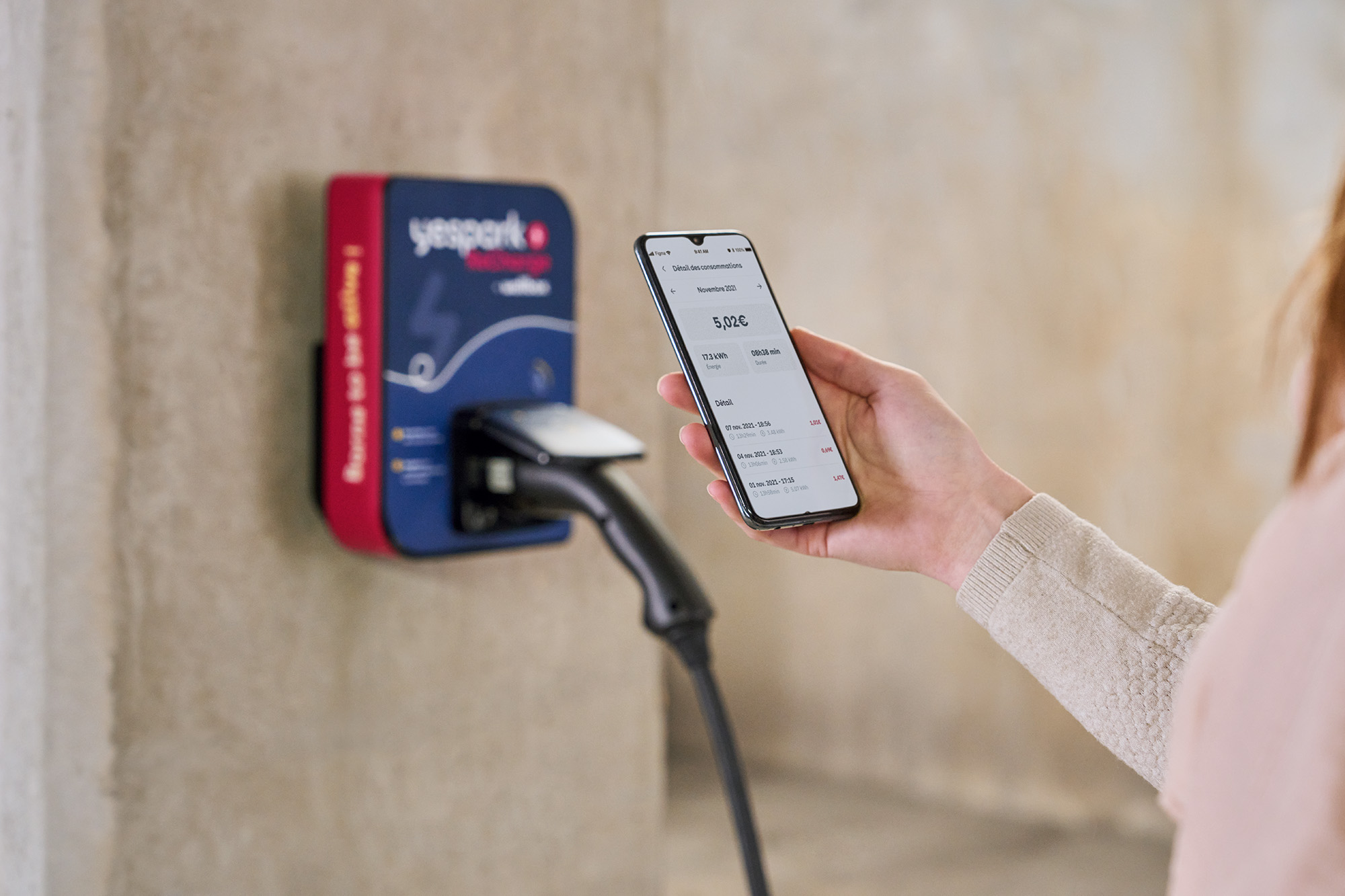 Pessoa a consultar o detalhe dos seus consumos na aplicação, em frente a um posto de carregamento Yespark ReCharge
