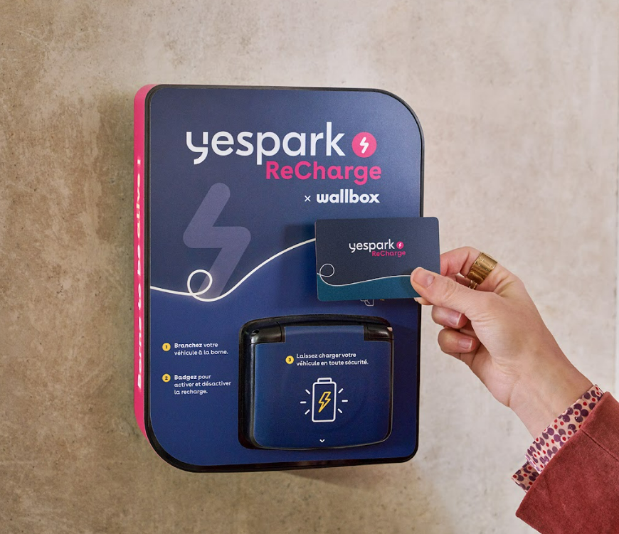 Hand holding the Yespark ReCharge badge in front of the Wallbox charging station's reader area