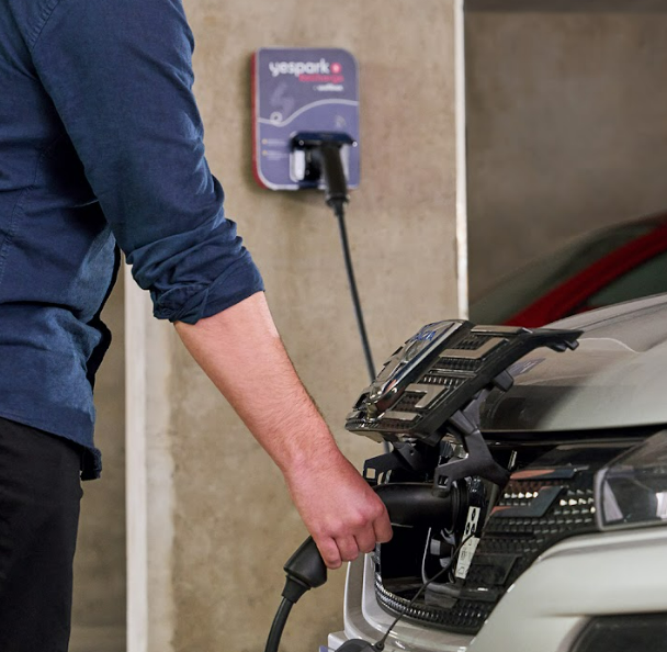Condutor a segurar o conector de carregamento do seu carro elétrico, ligado a um posto de carregamento Yespark de parede